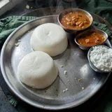 Two steamed idli on a steel plate with sambar and coconut chutney